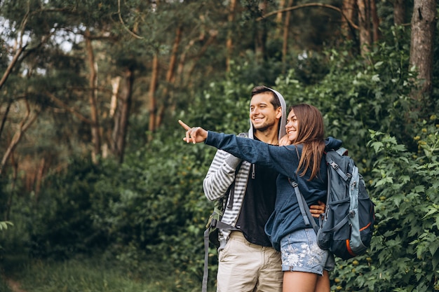 Pareja joven con mochilas en la espalda sonriendo y caminando en el bosque, disfruta del paseo