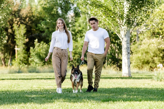 Pareja joven y moderna caminando y jugando con su perro Border Collie en un parque