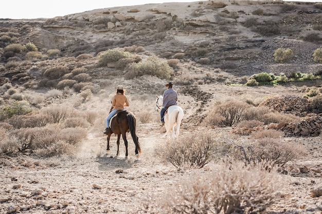 Pareja joven montando a caballo haciendo excursión al atardecer - El foco principal en la espalda de la mujer