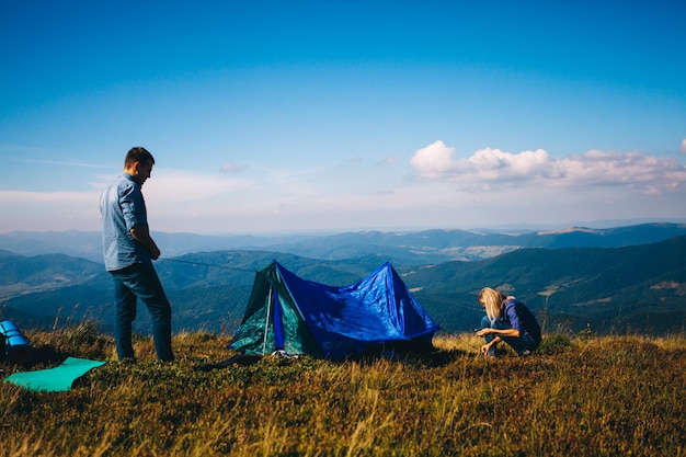 Pareja joven montando carpa en las montañas. Senderismo y acampada.