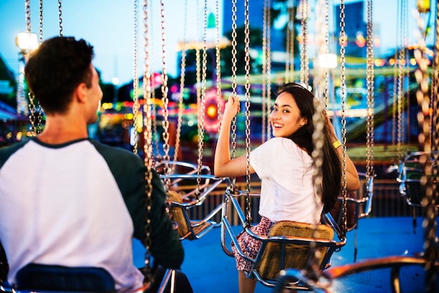 Foto pareja joven montando los columpios en un parque de diversiones