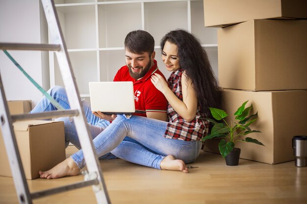 Pareja joven moviéndose en casa nueva. Sentado y relajándose después de desempacar. Mirando algo en la computadora portátil. Pareja joven