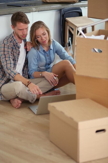 Pareja joven mudándose a un nuevo hogar. Sentarse y relajarse después de desempacar. Mirando algo en la computadora portátil. Pareja joven.