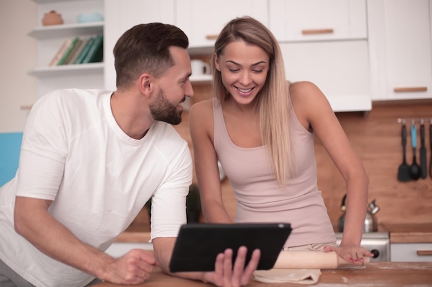 Pareja joven navegando por la web con tableta en la cocina de casa