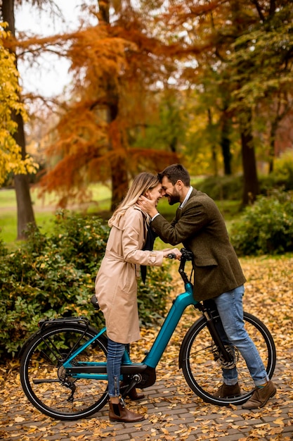 Pareja joven en el parque de otoño con bicicleta eléctrica