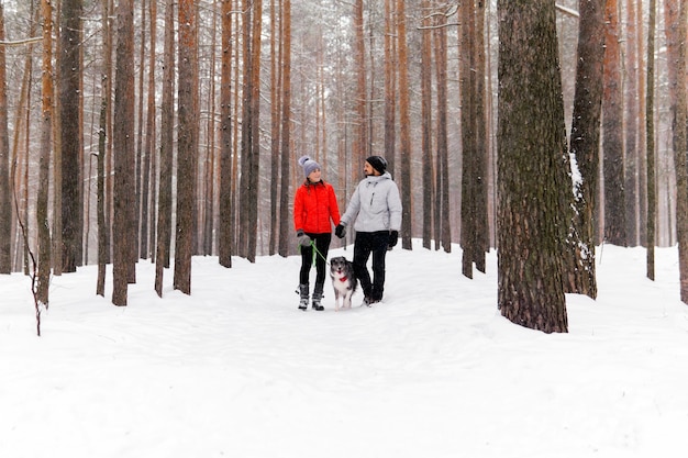 Pareja joven paseando a un perro en un bosque nevado de invierno