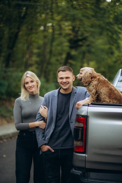 una pareja joven con un perro cocker spaniel cerca de un jeep en un bosque otoñal