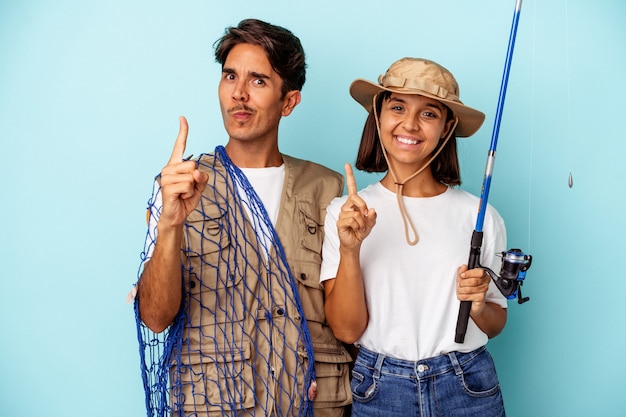 Pareja joven pescador de raza mixta aislado sobre fondo azul que muestra el número uno con el dedo.