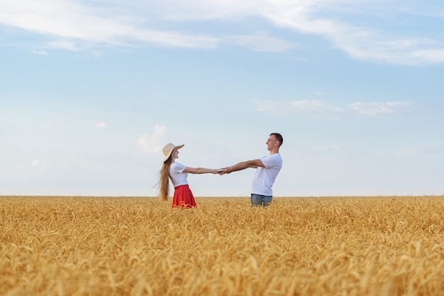 Pareja joven de pie en medio del campo de trigo y cogidos de la mano. Romance del campo