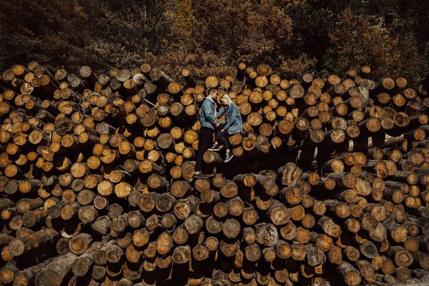 Pareja joven de pie sobre la pila de leña en el hermoso bosque de otoño colorido