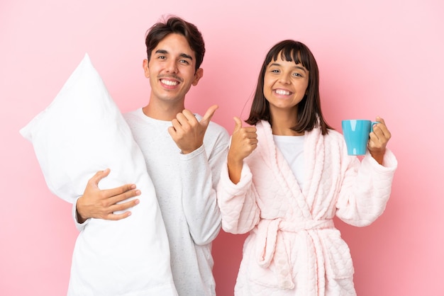 Una pareja joven en pijama aislada de fondo rosa dando un gesto de aprobación con ambas manos y sonriendo