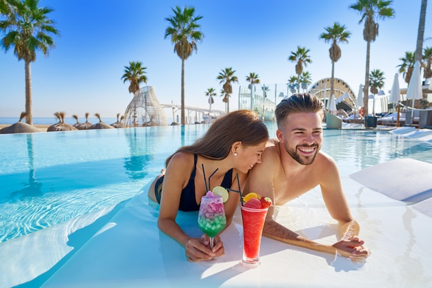 Pareja joven en piscina infinita cócteles