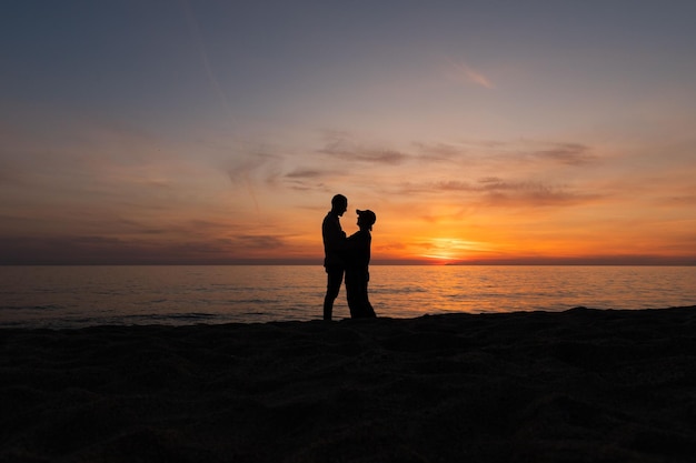 Pareja joven, posando con luz de fondo en una puesta de sol en la playa