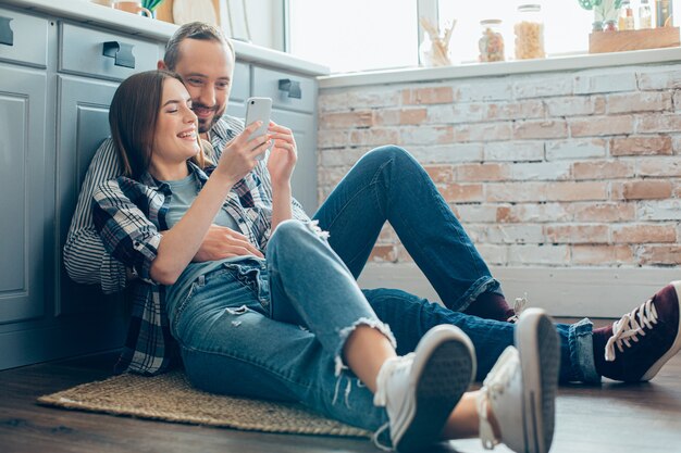 Pareja joven positiva abrazándose en el suelo de la cocina y mirando divertido