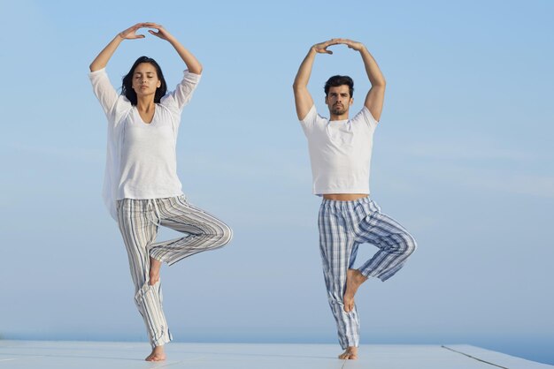 pareja joven practicando yoga al atardecer en una moderna terraza casera con océano y puesta de sol en el fondo