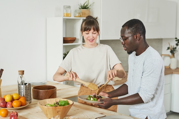 Pareja joven preparando ensalada de verduras juntos en la cocina