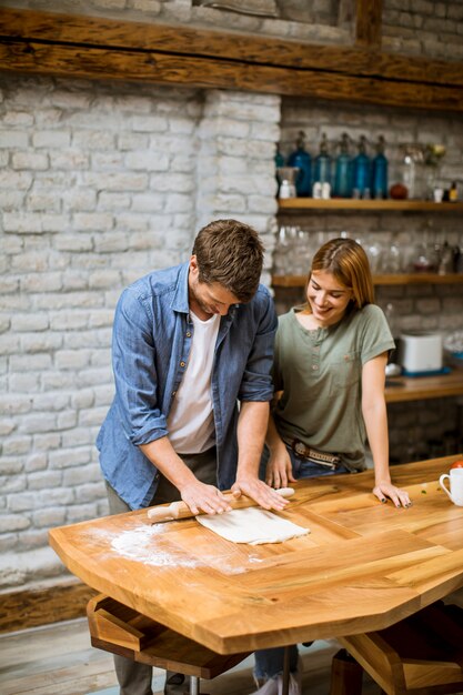 Pareja joven preparando masa en casa en la cocina rústica