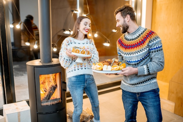 Pareja joven preparándose para la cena festiva llevando comidas en la casa moderna durante las vacaciones de invierno