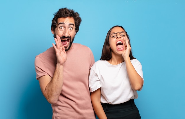 Pareja joven que se siente feliz, emocionada y positiva, dando un gran grito con las manos al lado de la boca, gritando