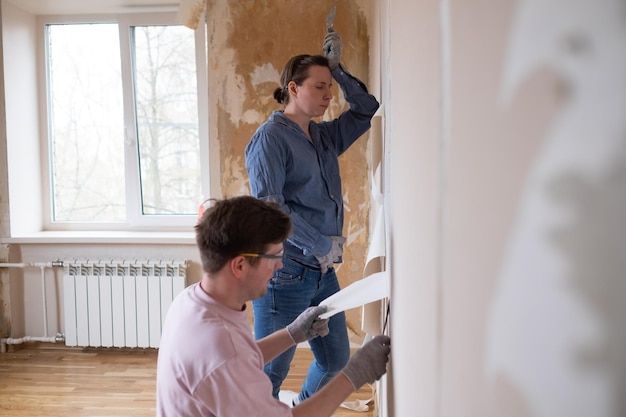 Pareja joven quitando papel tapiz viejo de las paredes preparándose para la renovación plana