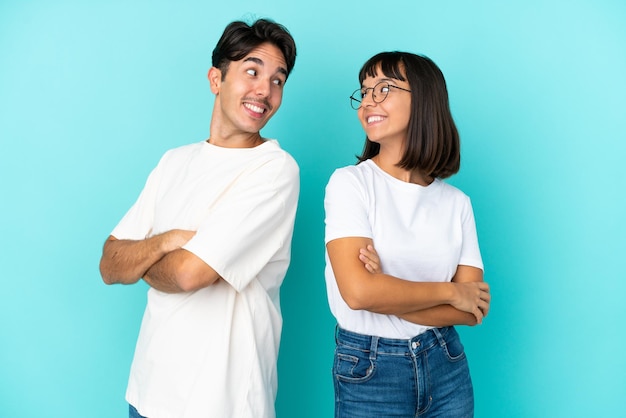 Pareja joven de raza mixta aislado sobre fondo azul mirando por encima del hombro con una sonrisa