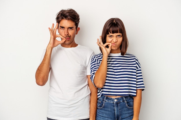 Pareja joven de raza mixta aislado sobre fondo blanco con los dedos en los labios manteniendo un secreto.