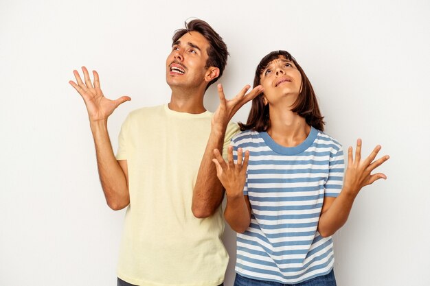 Pareja joven de raza mixta aislado sobre fondo blanco gritando al cielo, mirando hacia arriba, frustrado.