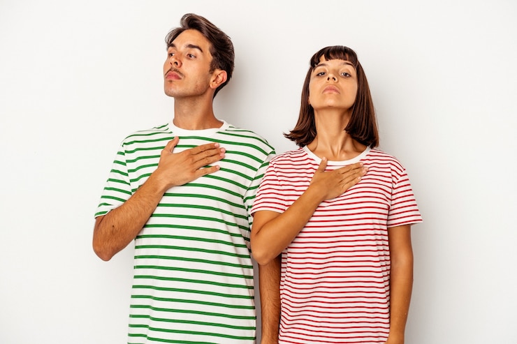 Foto pareja joven de raza mixta aislado sobre fondo blanco tomando un juramento, poniendo la mano en el pecho.