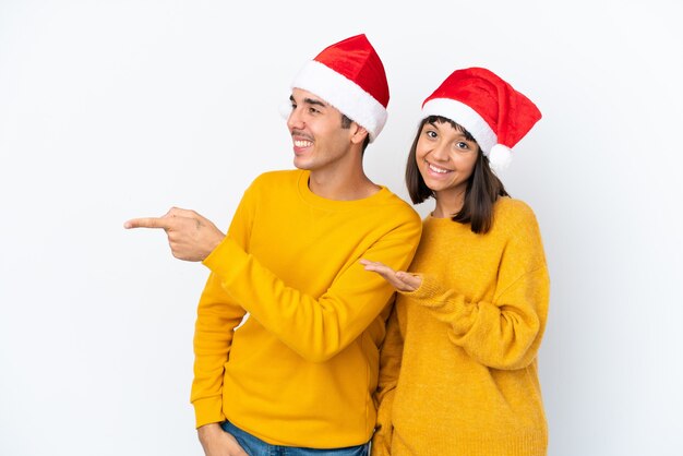 Pareja joven de raza mixta celebrando la Navidad aislado sobre fondo blanco apuntando hacia atrás y presentando un producto