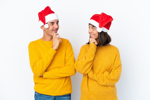 Pareja joven de raza mixta celebrando la Navidad aislado sobre fondo blanco mirando el uno al otro