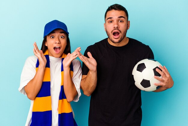 Foto pareja joven de raza mixta limpieza de casa aislada en azul sorprendido y conmocionado.