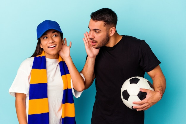 Foto pareja joven de raza mixta limpieza de casa aislado sobre fondo azul tratando de escuchar un chisme.