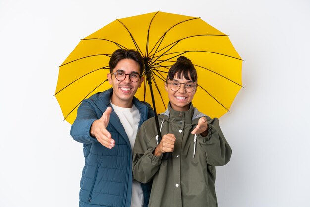 Foto pareja joven de raza mixta sosteniendo un paraguas aislado sobre fondo blanco un apretón de manos para cerrar un buen trato