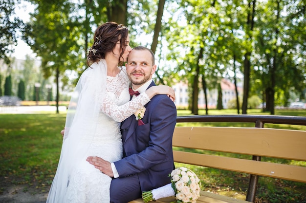 Pareja joven recién casados besándose en un banco del parque