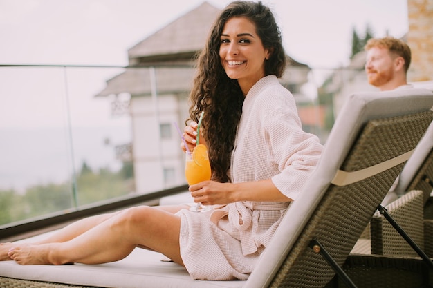 Una pareja joven relajándose en las camas y bebiendo jugo de naranja fresco en la terraza al aire libre