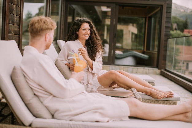 Una pareja joven relajándose en las camas y bebiendo jugo de naranja fresco en la terraza al aire libre