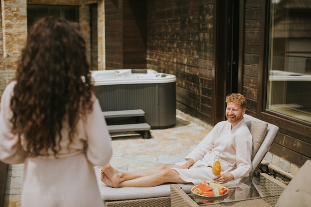 Una pareja joven relajándose en las camas y bebiendo jugo de naranja fresco en la terraza al aire libre