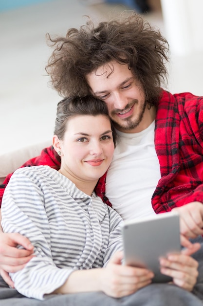 Foto una pareja joven relajándose en casa usando tabletas leyendo en la sala de estar en el sofá cama.