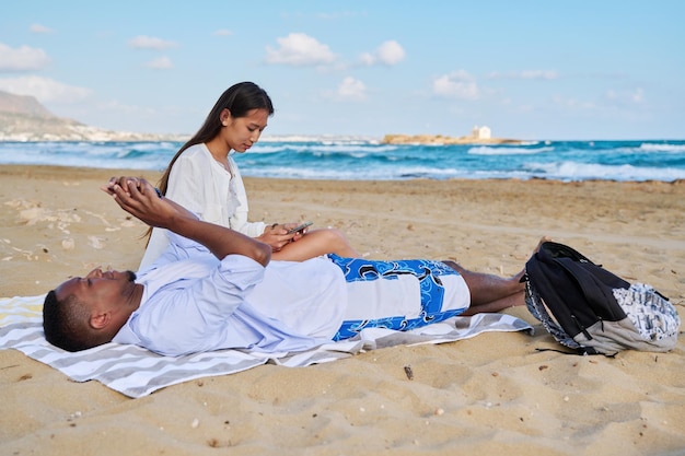 Una pareja joven relajándose en la playa tumbada sentada en la arena con smartphones