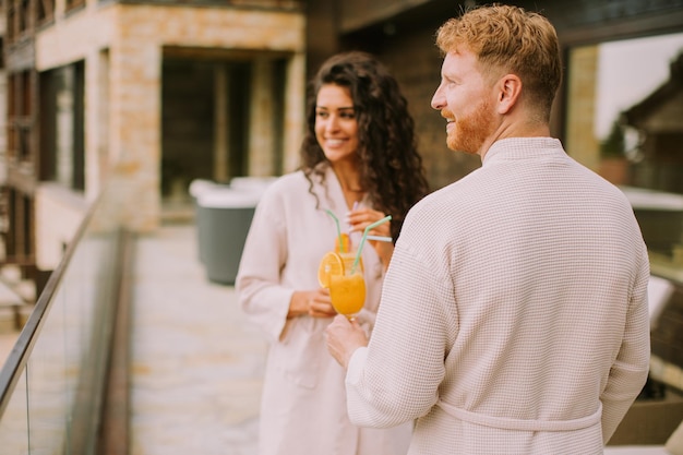 Pareja joven relajándose en la terraza al aire libre y bebiendo jugo de naranja fresco