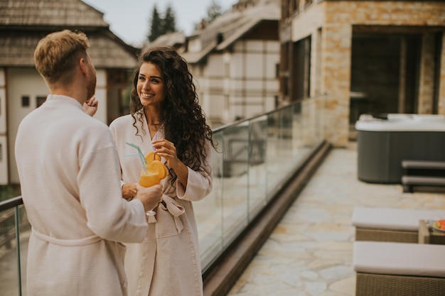 Pareja joven relajándose en la terraza al aire libre y bebiendo jugo de naranja fresco