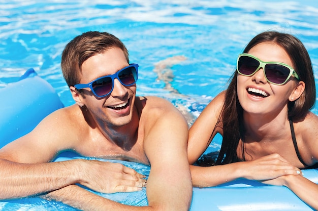 Pareja joven relajarse en el agua azul de la piscina en verano