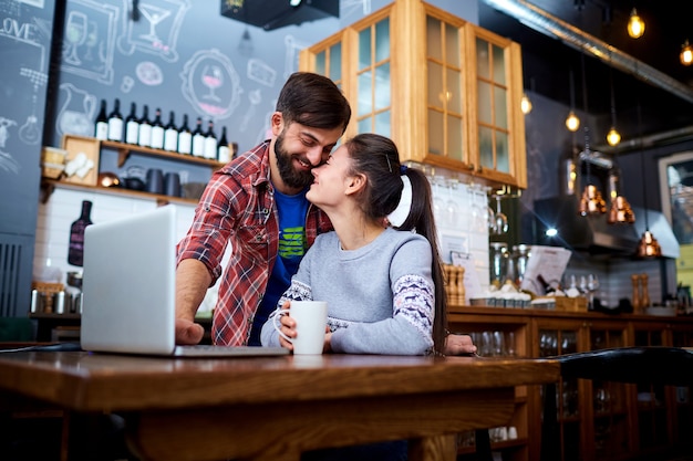 Pareja joven en un restaurante cafetería con portátil sonriendo a la mesa.