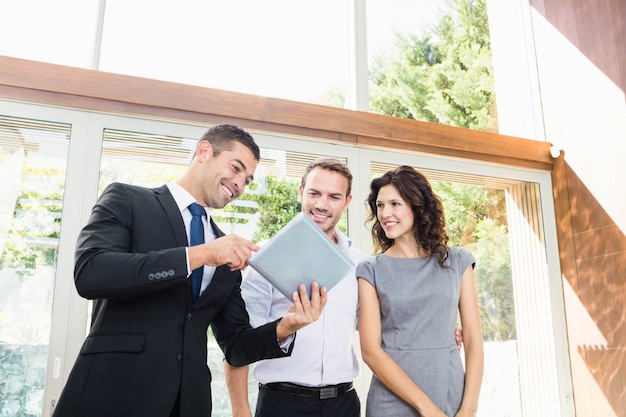 Pareja joven reunión inmobiliaria mostrando un proyecto de casa en una tableta digital