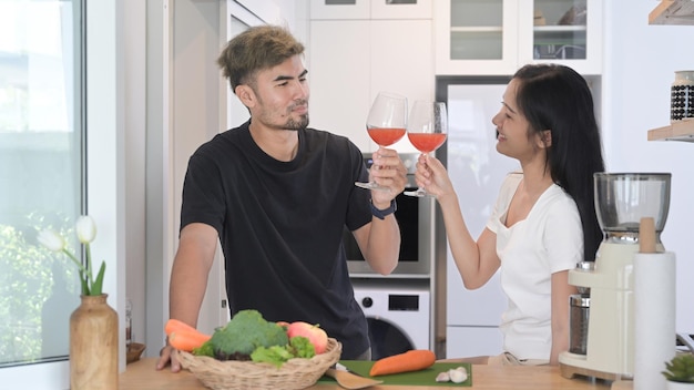 Pareja joven romántica preparando comida saludable y bebiendo vino en la cocina casera moderna