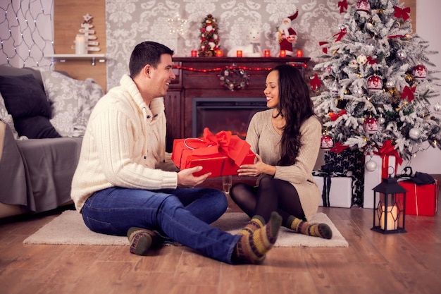 Pareja joven romántica sentada frente a una chimenea el día de Navidad. Regalo de Navidad. Adornos navideños tradicionales.