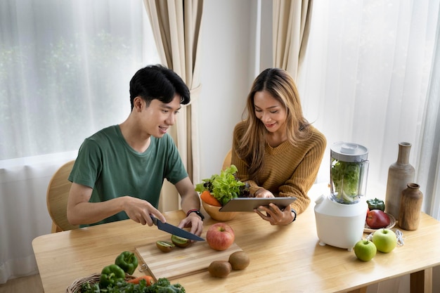 Pareja joven saludable preparando ingredientes para hacer batido de desintoxicación de verduras verdes en la cocina