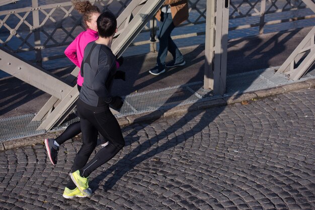 Una pareja joven y saludable trotando en la ciudad a primera hora de la mañana con el amanecer en segundo plano.