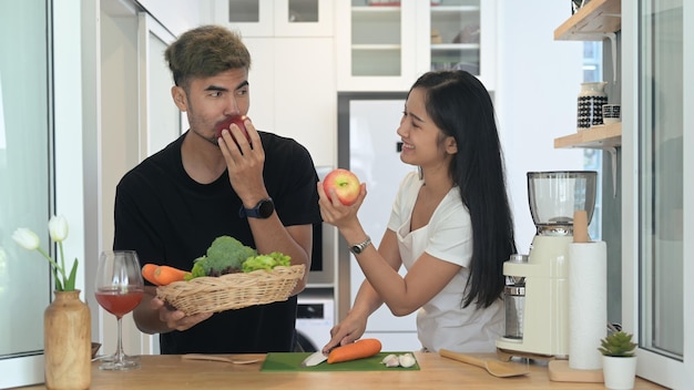 Una pareja joven y sana disfruta haciendo un batido de desintoxicación verde con verduras y frutas frescas en la cocina