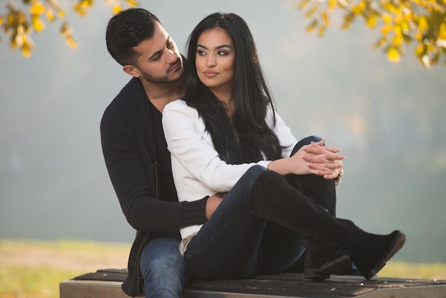 Pareja joven sentada en un banco en el hermoso día de otoño